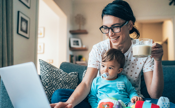 mom looking at laptop with cup of coffee while holding a baby in her lap